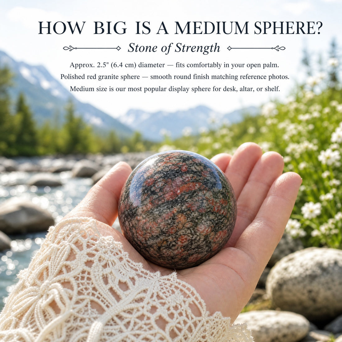 A polished red granite sphere, speckled red, black and grey, resting in an open palm beside a mountain stream