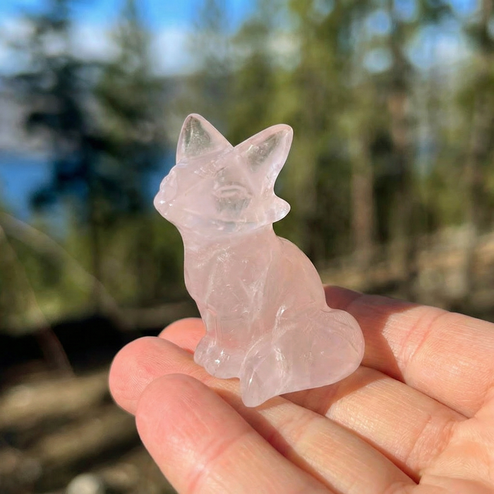 The hand-carved rose quartz fox sitting upright on an open palm