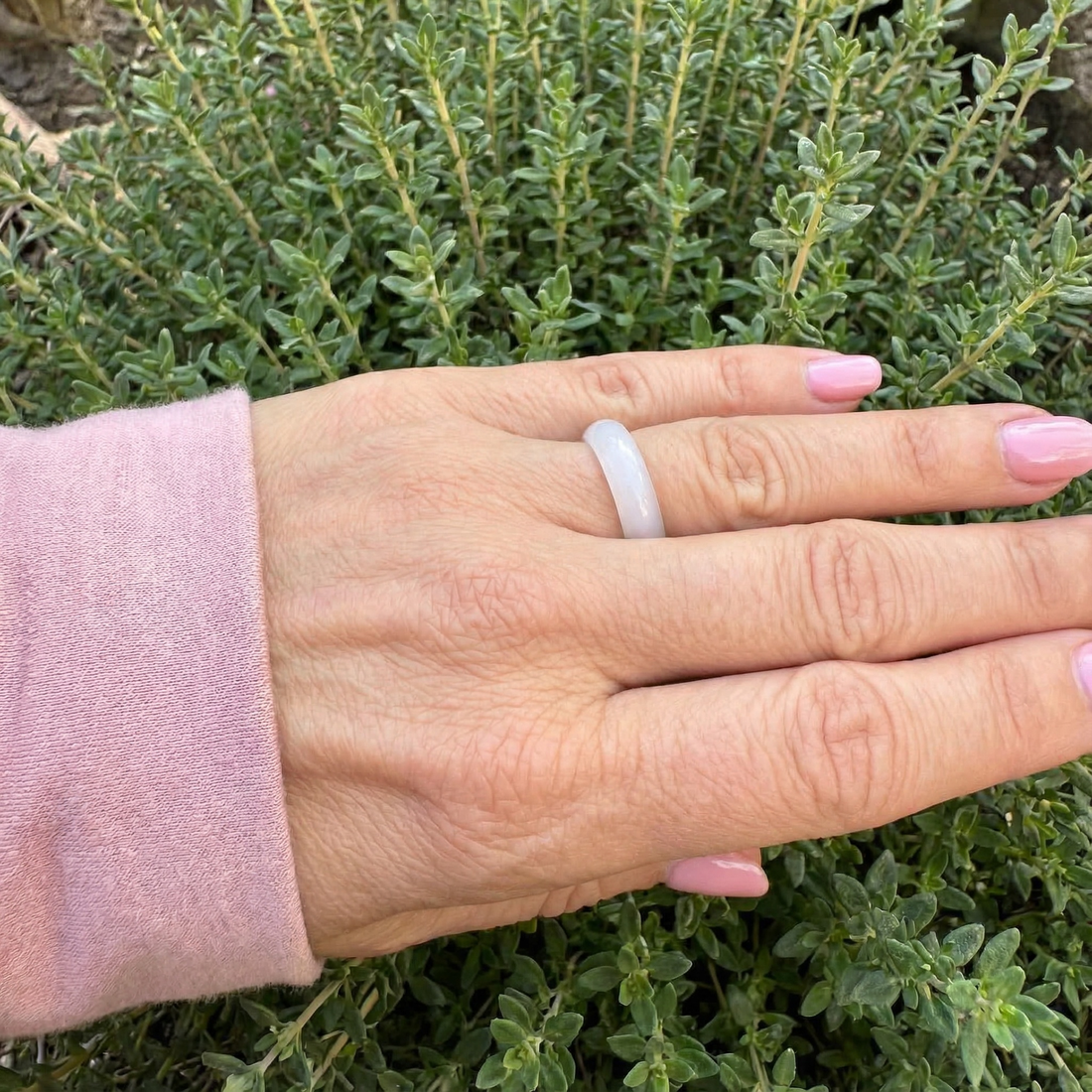 A pale pink agate ring worn on a finger, the hand resting on green thyme