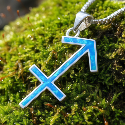 Close-up of the Sagittarius arrow glyph pendant inlaid with blue opal in a sterling silver setting, resting on moss
