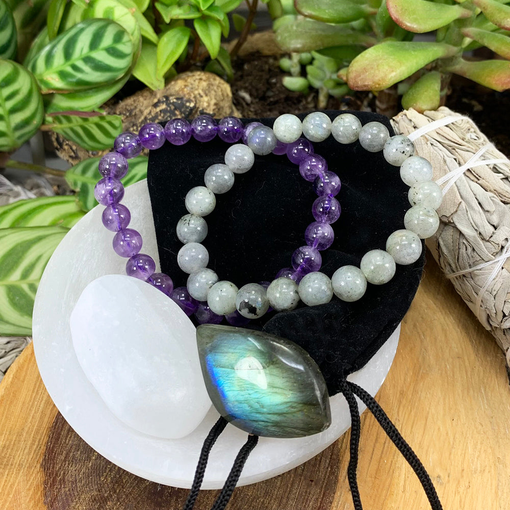 Amethyst and labradorite mala bracelets on a black velvet pouch with a white selenite ellipse and a blue-flashing labradorite cabochon