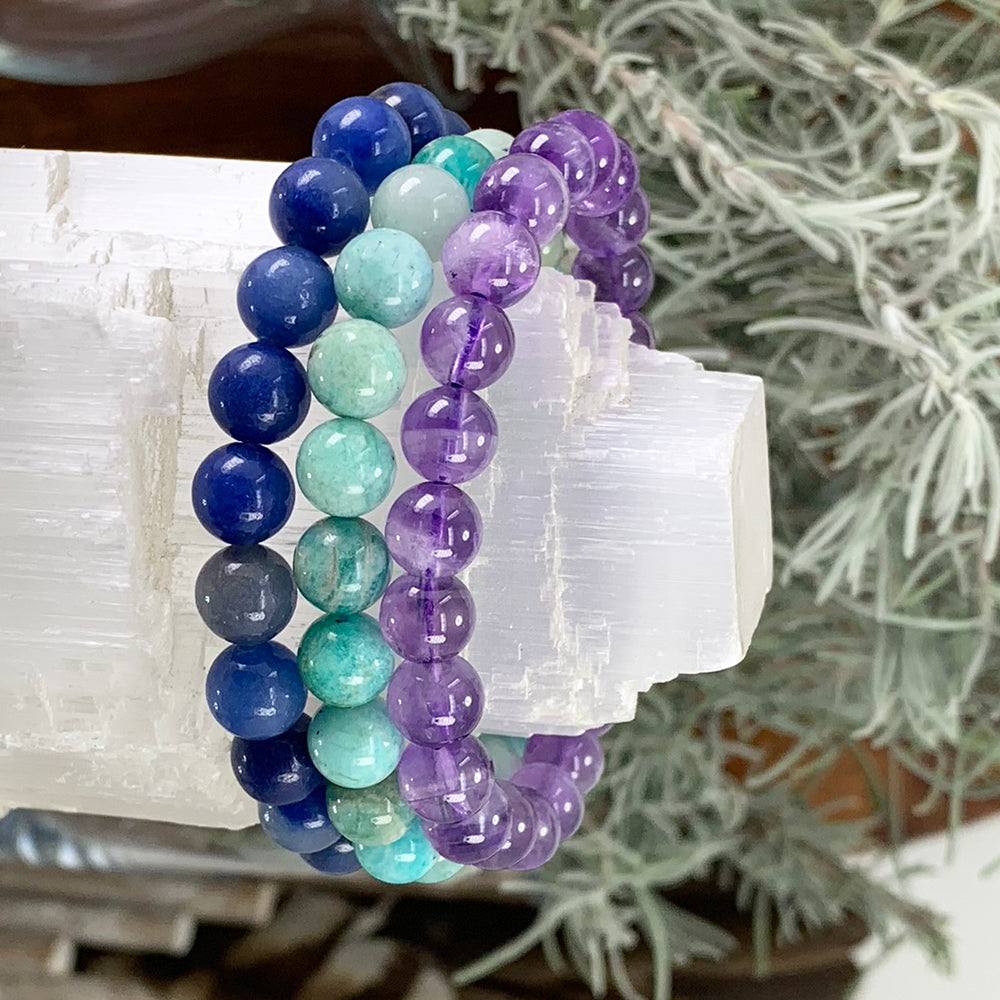 Blue aventurine, amazonite and amethyst bead bracelets stacked together on a white selenite block