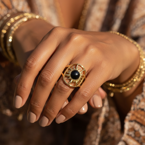 The solar power ring worn on a hand with gold bangles, its black onyx and gold sunburst sitting across the finger