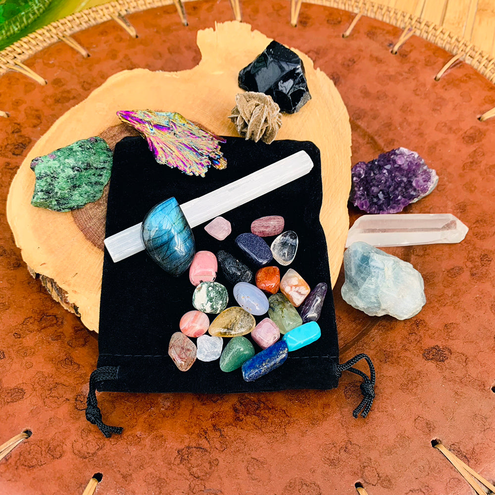 The full collection laid out on a wood slice: nine larger specimens around a black velvet pouch scattered with twenty tumbled mini gemstones