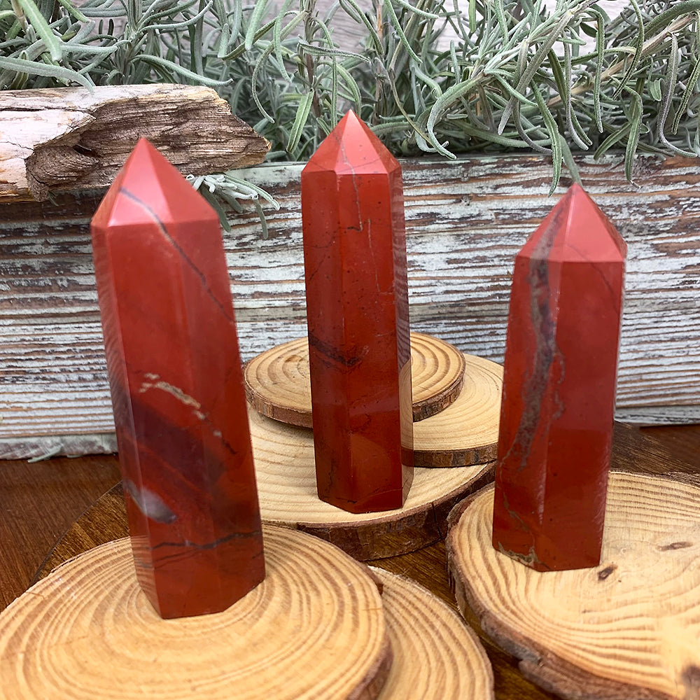 Three polished red jasper points with dark veins and banding standing on wood slices