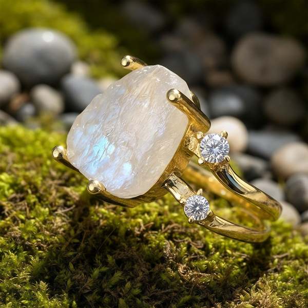 Close-up of the moonstone and gold ring on moss: a glowing moonstone held in gold claws on a split gold band