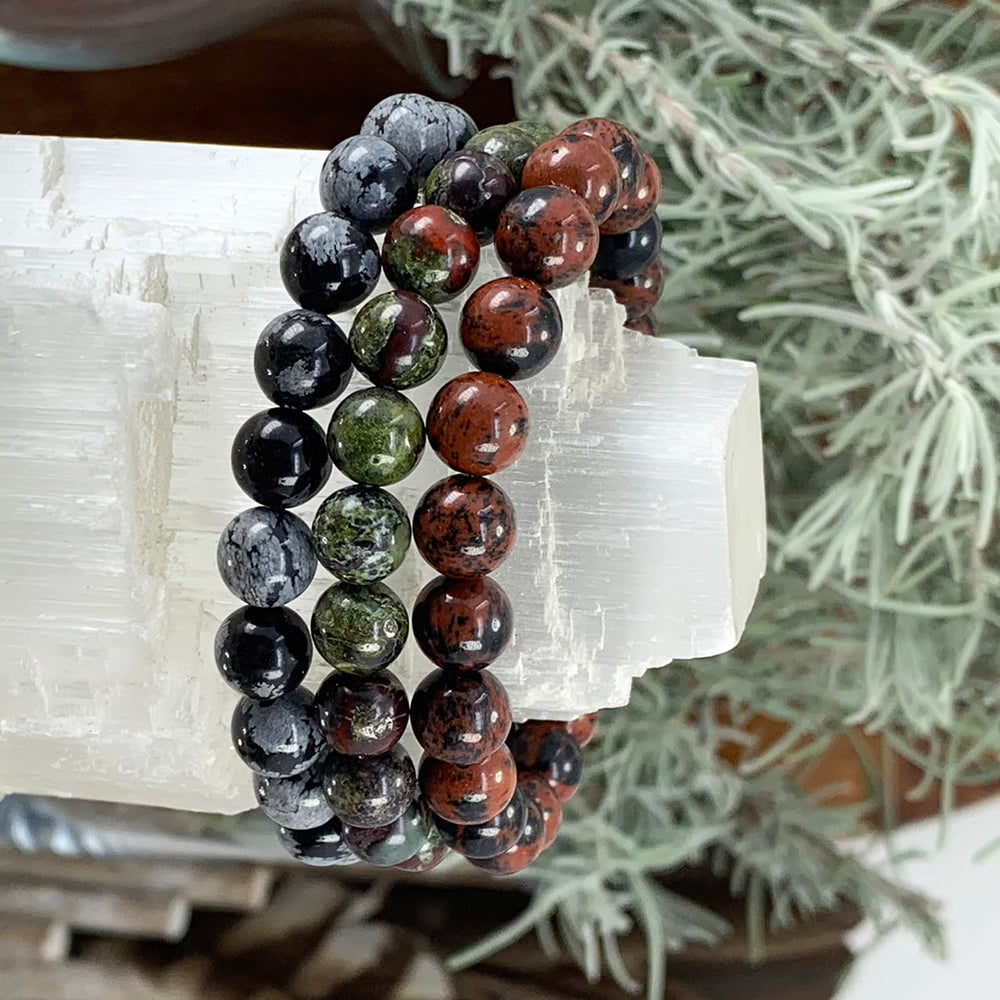 Snowflake obsidian, dragon’s blood and red obsidian bead bracelets stacked together on a white selenite block