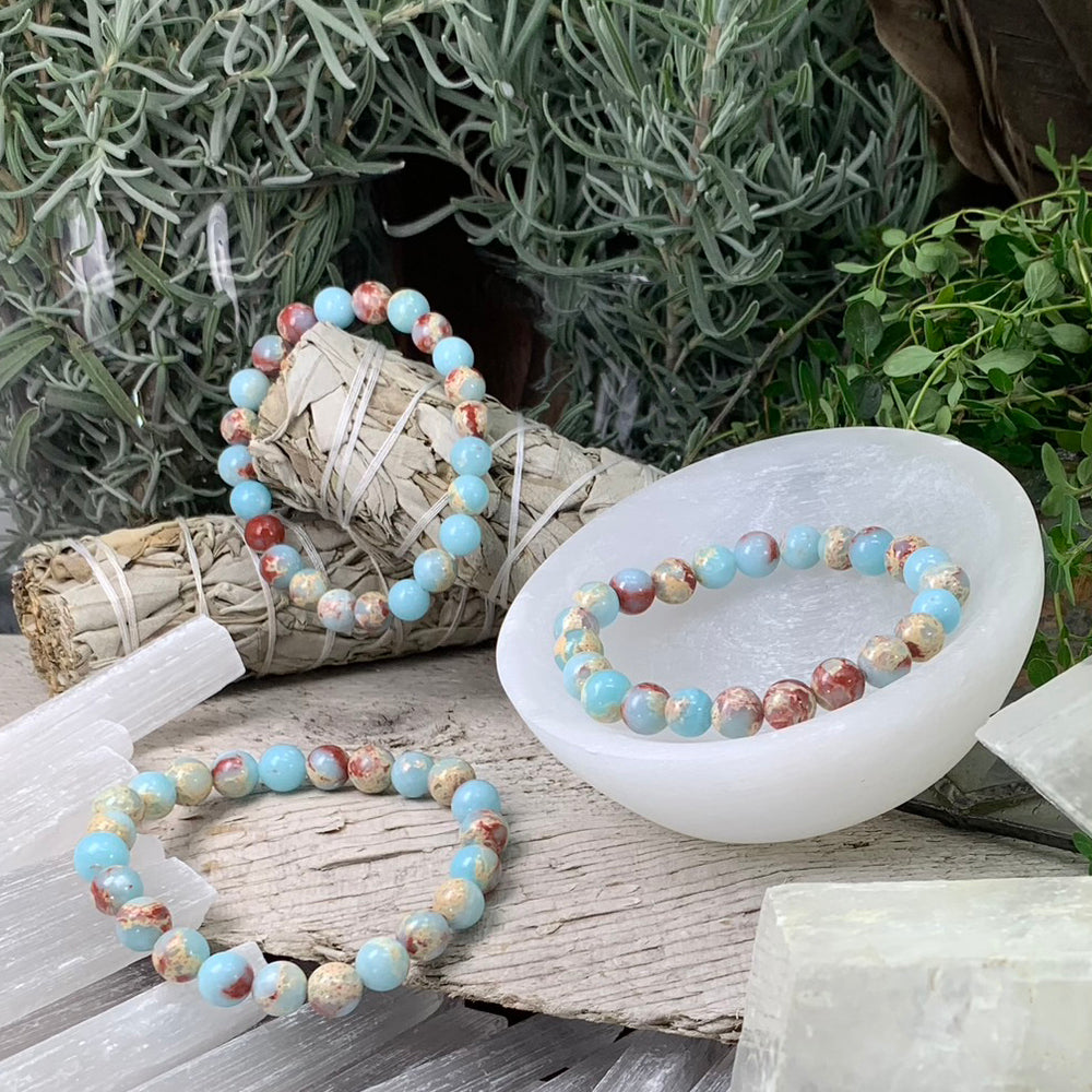 Azure variscite mala bracelets of round sky blue beads marbled with rust red and cream, one resting in a white selenite bowl