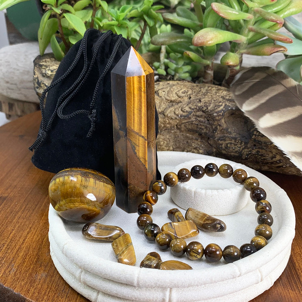 Golden-brown tiger eye point, tumbled stone, bead bracelet and mini stones on a white dish, with a black velvet pouch behind