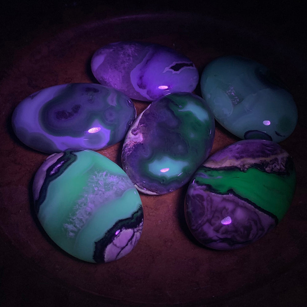 Volcanic agate palmstones under UV light, glowing in bands of bright green and violet