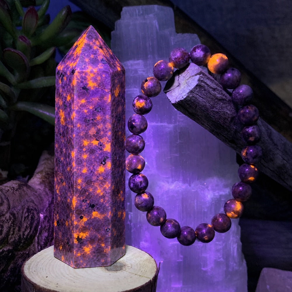 The same Yooperlite point and bracelet under UV light, glowing with bright orange speckles against purple stone