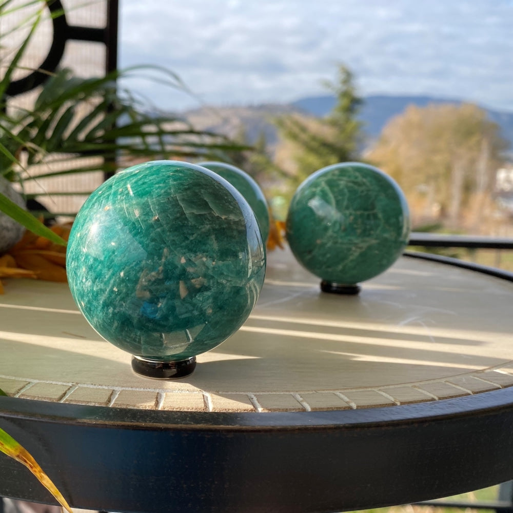 Polished amazonite spheres in aqua green with pale veining, resting on black stands on a sunny patio table