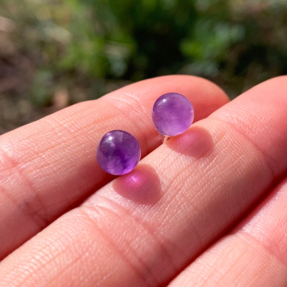 Two round polished amethyst studs resting on fingertips in sunlight