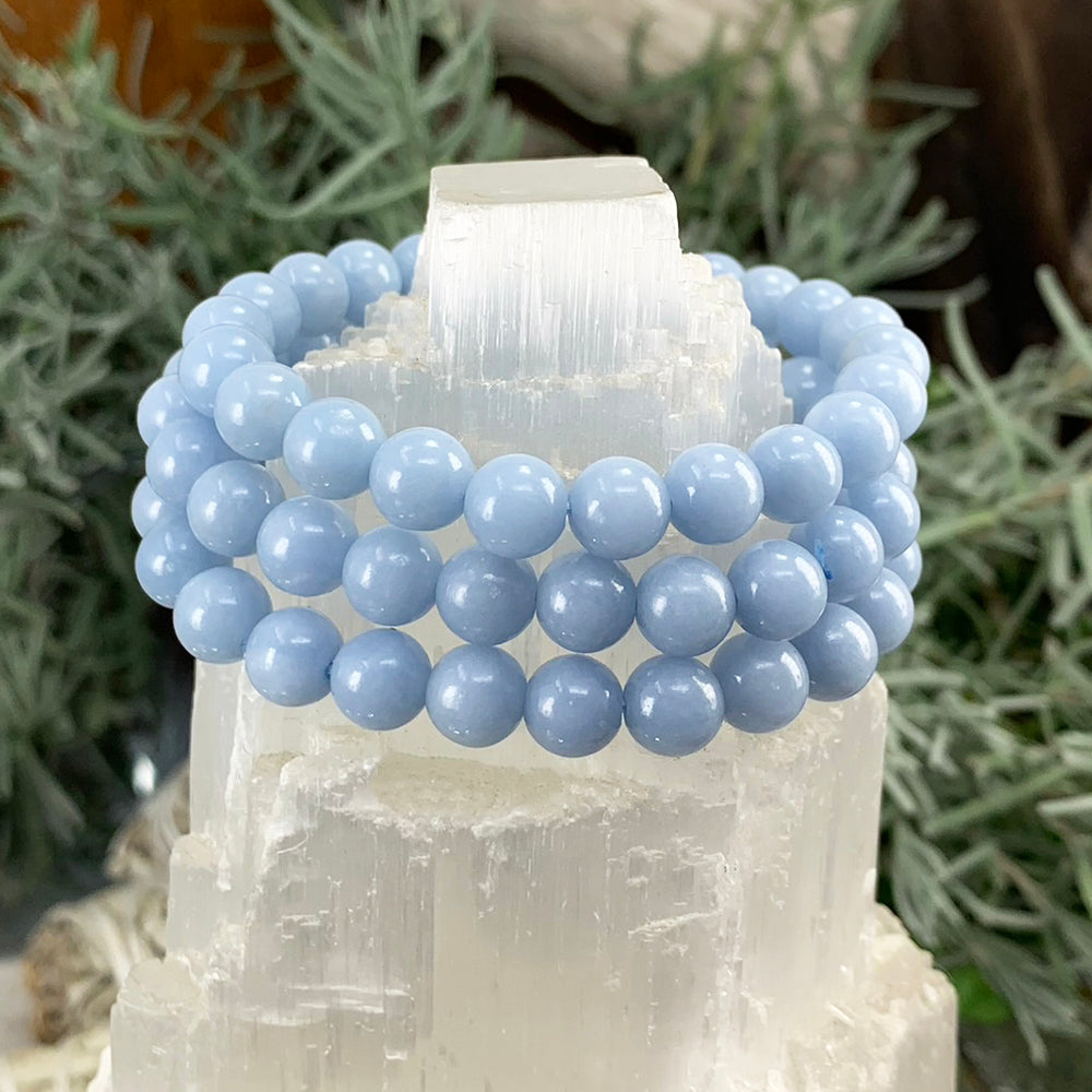 Several angelite bracelets stacked on a selenite tower, showing natural variation in the beads