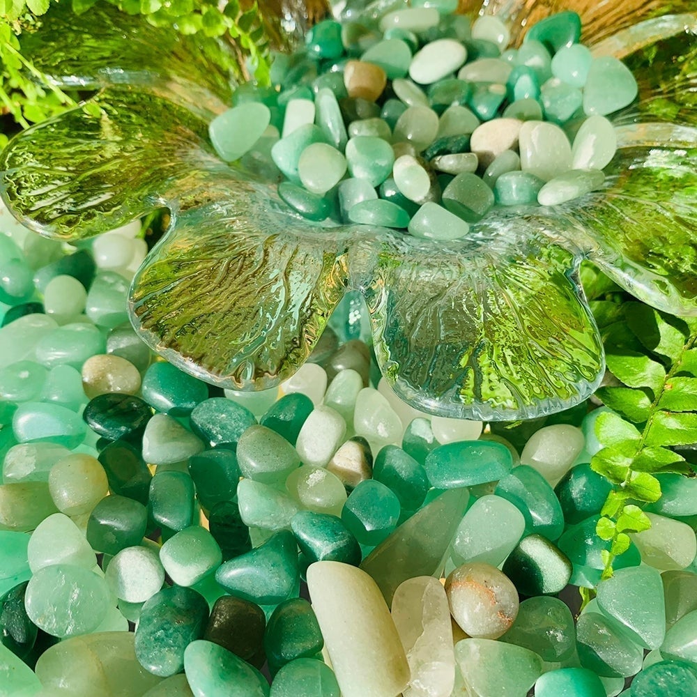 Green aventurine mini gemstones spilling around a clear glass leaf dish among ferns