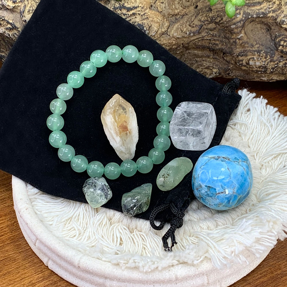 Green aventurine bead bracelet on a black velvet pouch with a citrine shard, clear quartz cube, blue apatite tumble and three pale green prehnite stones