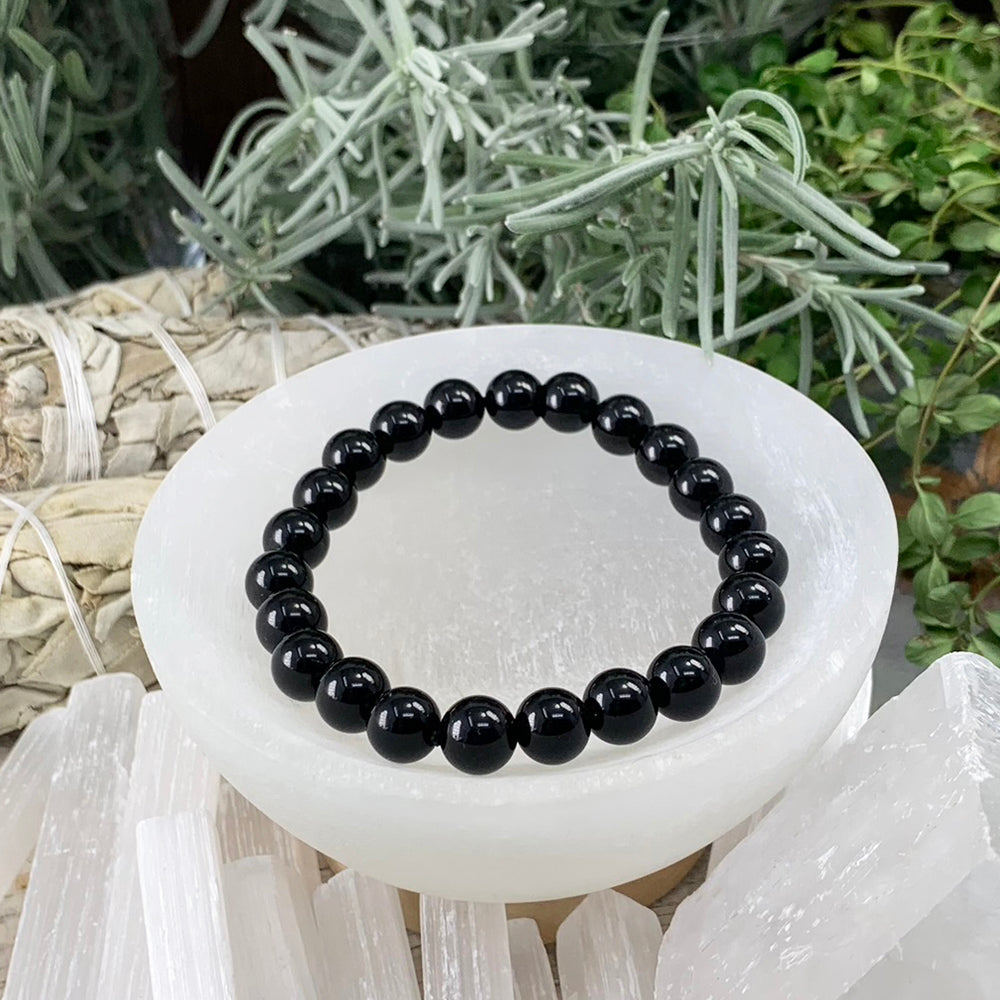 A single black obsidian mala bracelet of round glossy black beads resting in a selenite bowl