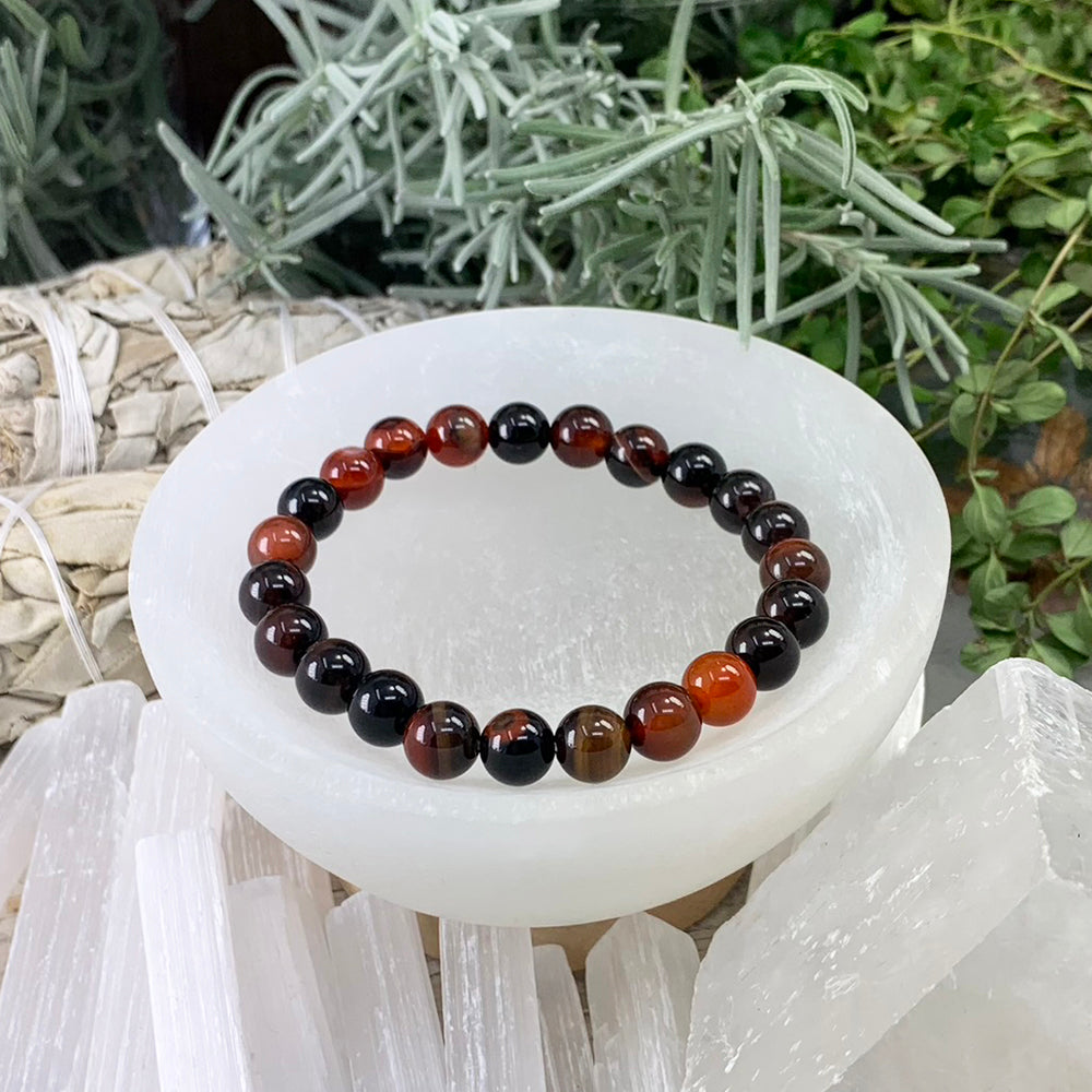 A black stripe agate bead bracelet of glossy black, deep red and amber beads resting in a selenite bowl