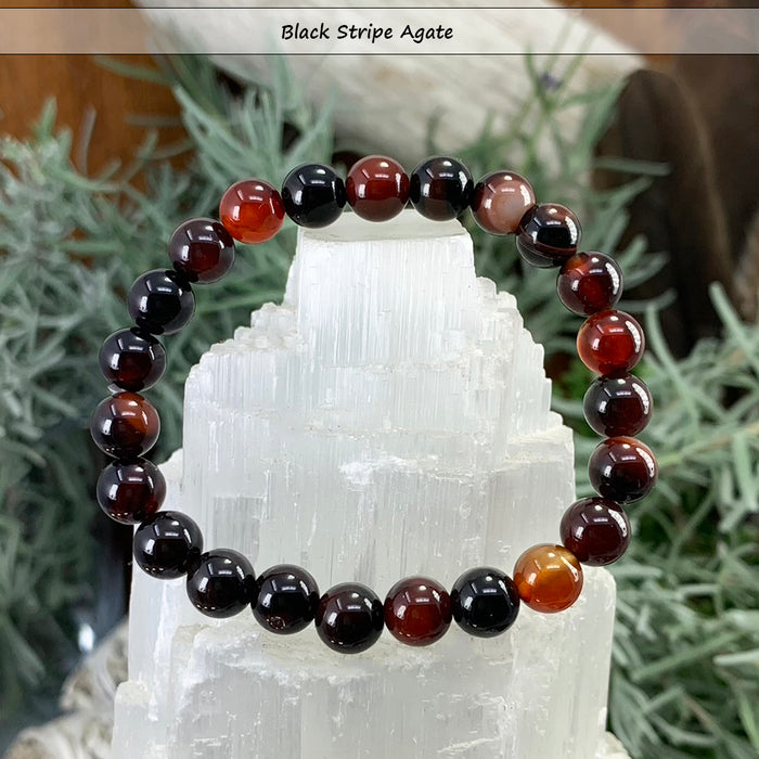 Black stripe agate bead bracelet in black, deep red and amber banded beads on a selenite tower