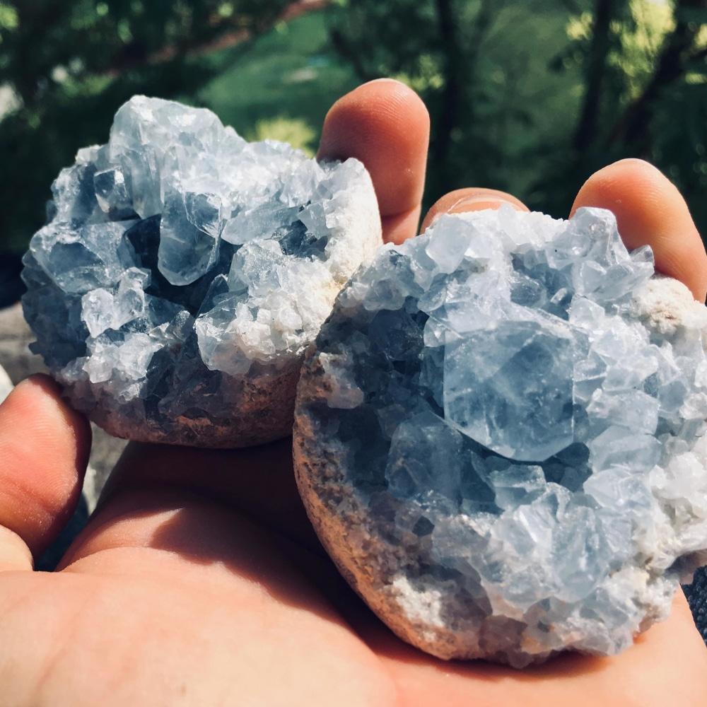 Two celestite geode halves resting together in an open palm outdoors