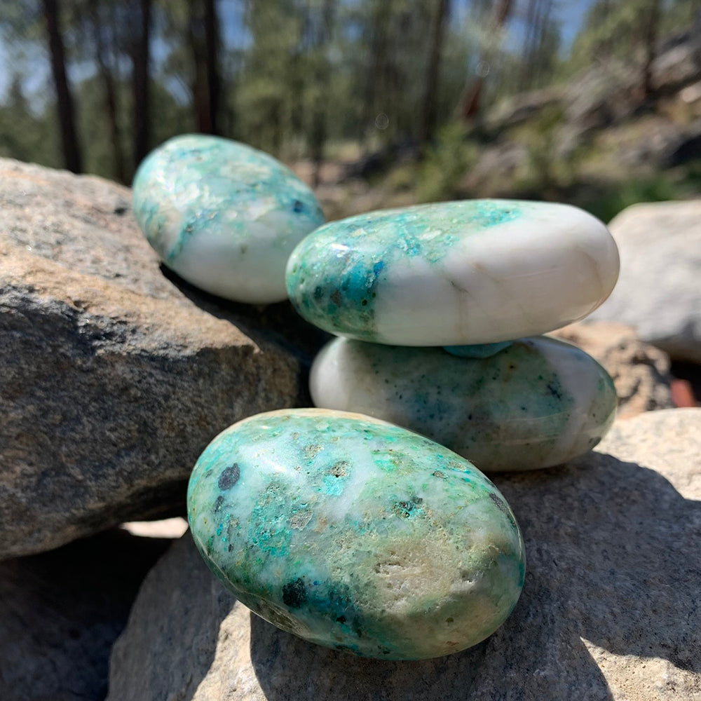 Four chrysocolla palmstones stacked on sunlit rocks, each with its own mix of teal, green and white
