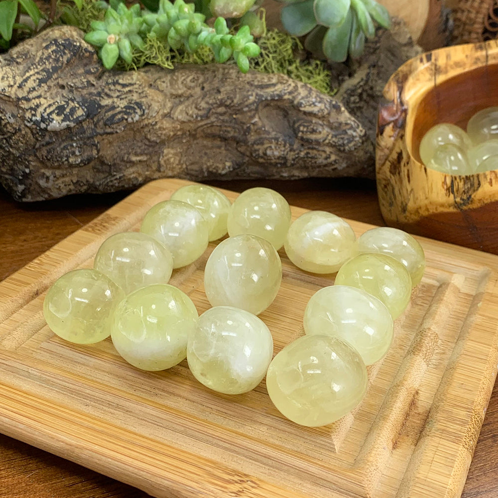 A batch of smooth, pale lemon-yellow tumbled citrine stones on a bamboo tray; each order includes one stone