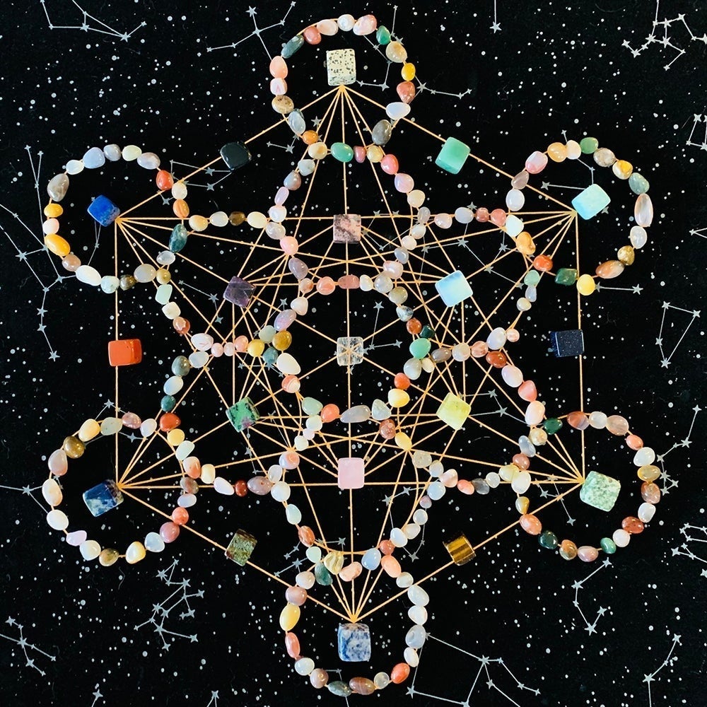 Top-down view of a Metatron cube crystal grid: agate rings with tumbled cubes and spheres placed on the gold lines of the velvet cloth