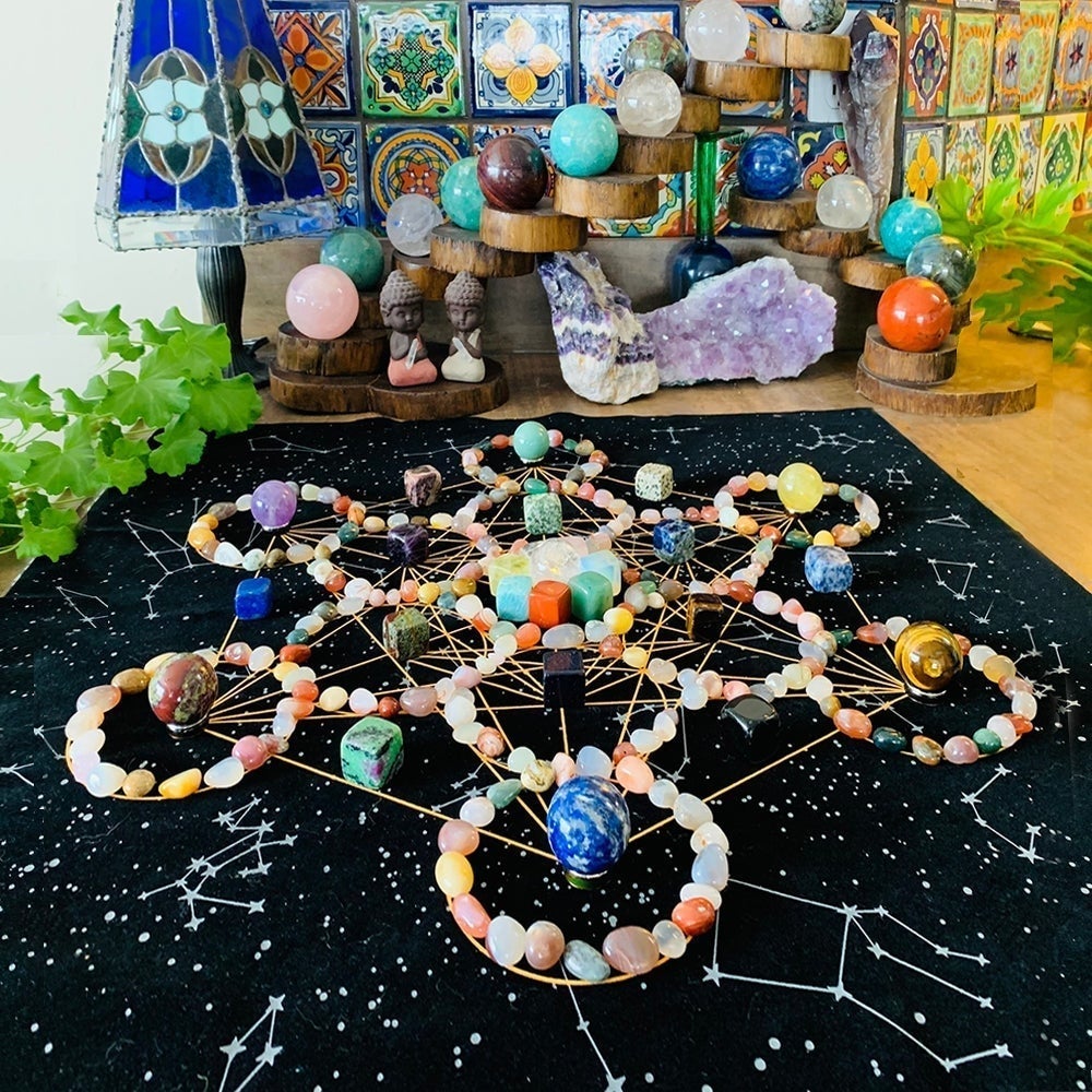A finished crystal grid of agate rings, tumbled stones and spheres laid out on a starry black velvet sacred geometry cloth on a table