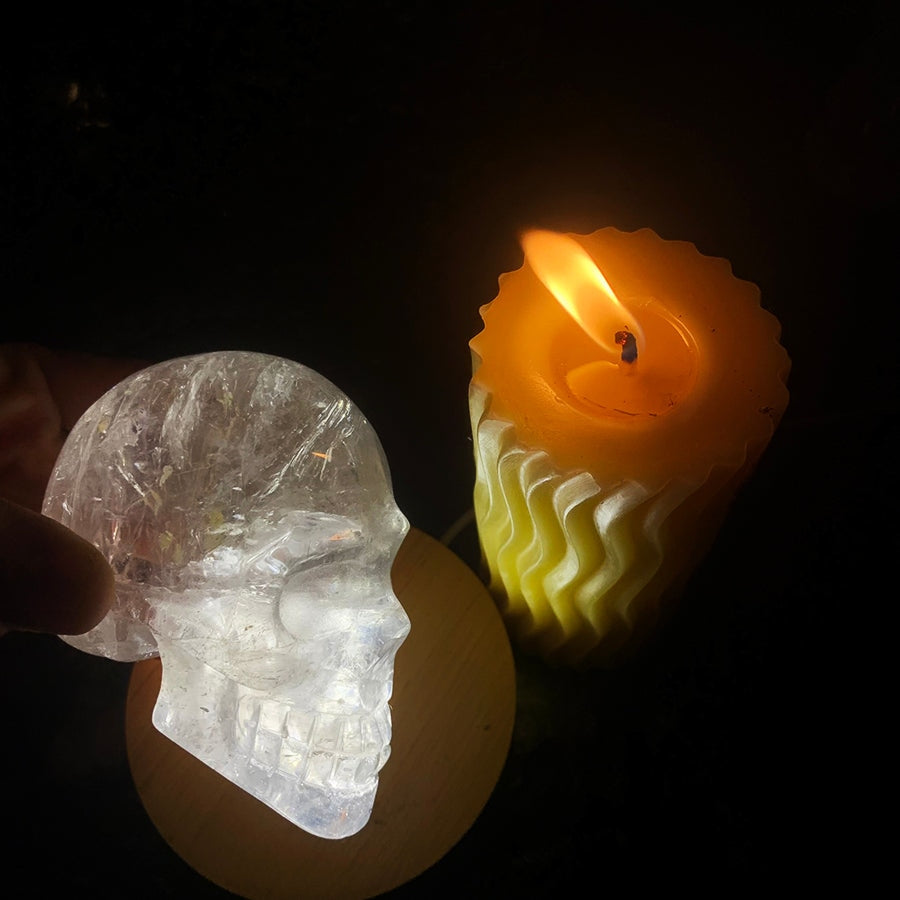 The clear quartz skull glowing beside a lit candle, its inner veils and fractures lit from within