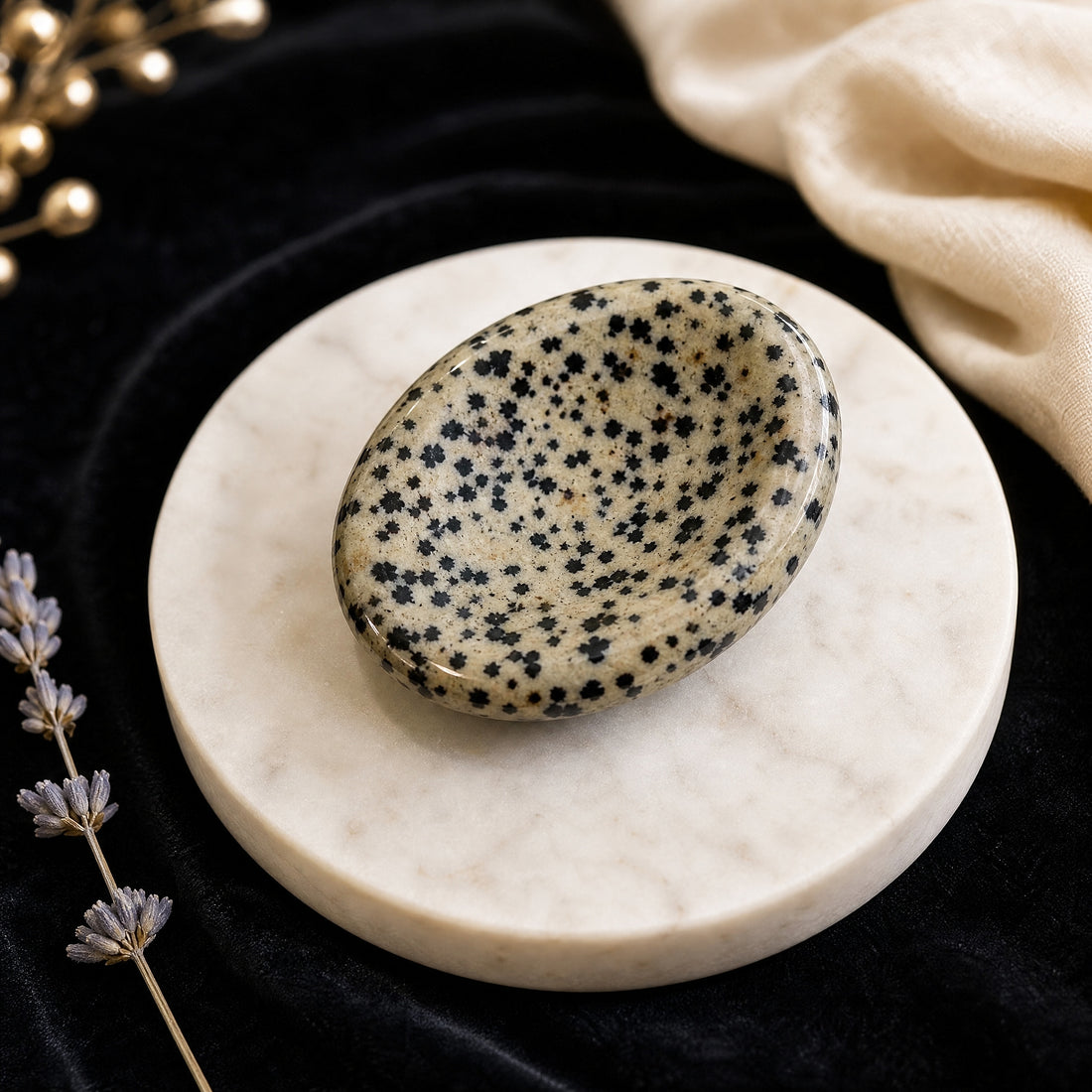 Polished oval Dalmatian Jasper worry stone, cream with black spots, resting on a marble dish