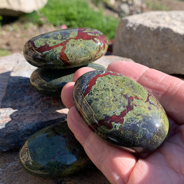 A smooth dragon blood palmstone resting in an open palm beside a stack of others