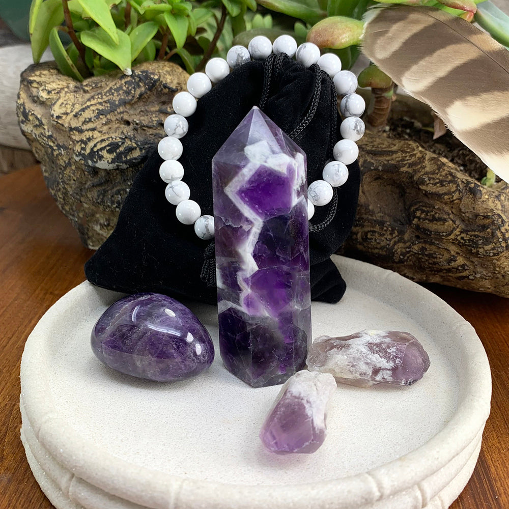 The full set on a white dish: a dream amethyst point, an oval dream amethyst stone, two amethyst shards, and a white howlite bead bracelet draped over a black velvet pouch