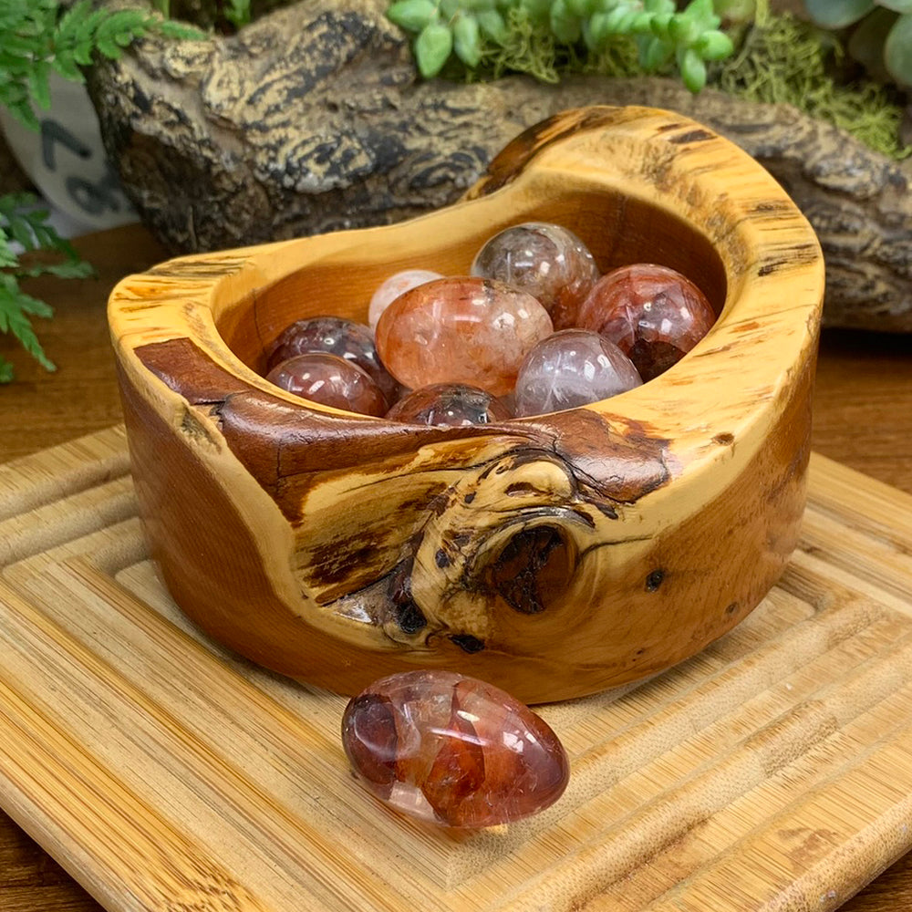 Polished fire quartz tumbled stones with red and orange hematite inclusions in a wooden bowl, with one resting in front