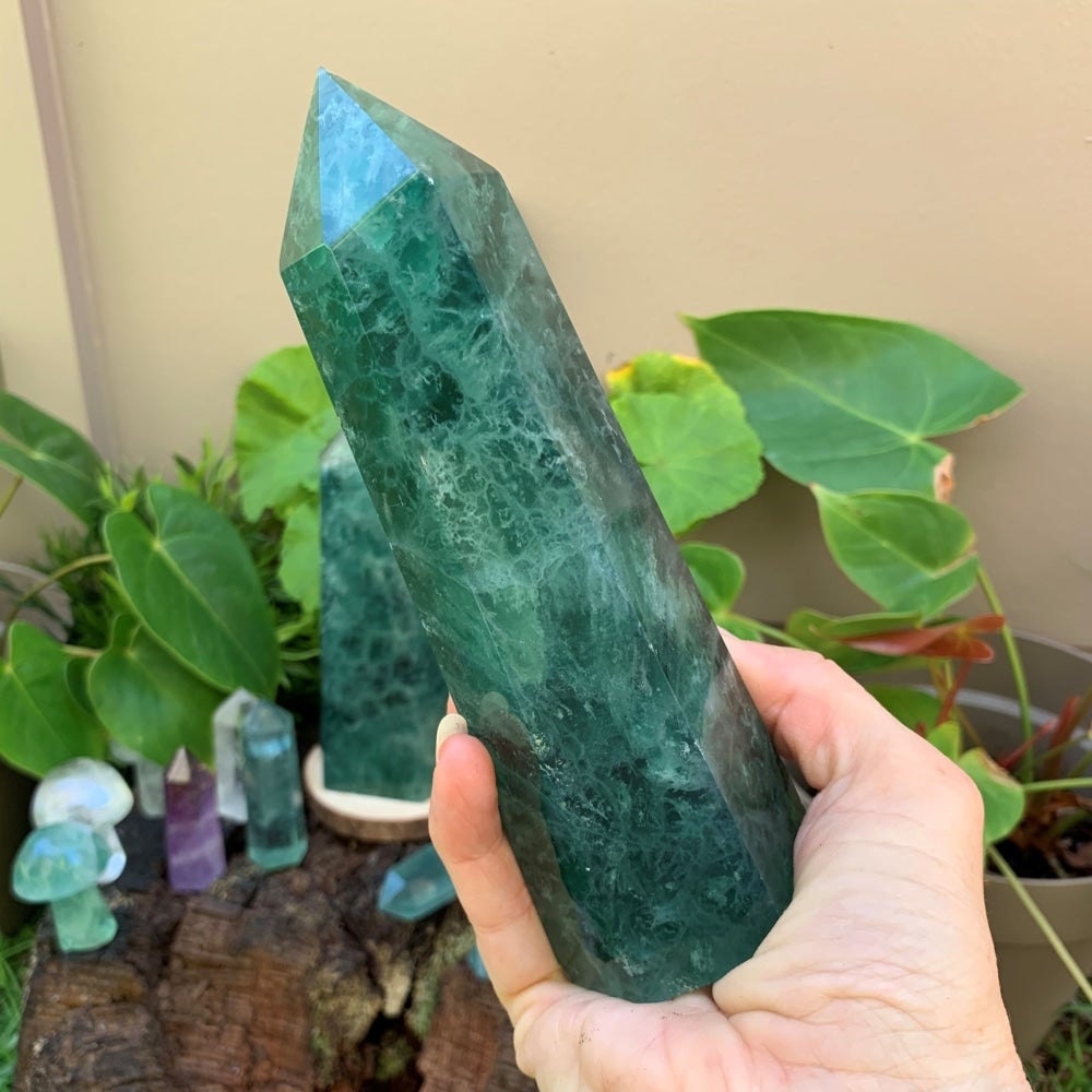 A hand holding a large green fluorite generator, its white and green veining visible inside