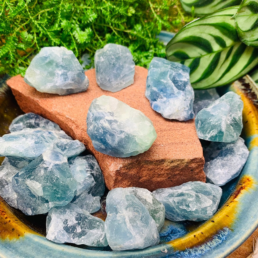 A selection of rough green fluorite pieces in sea green and blue-green, on a red stone block in a glazed bowl