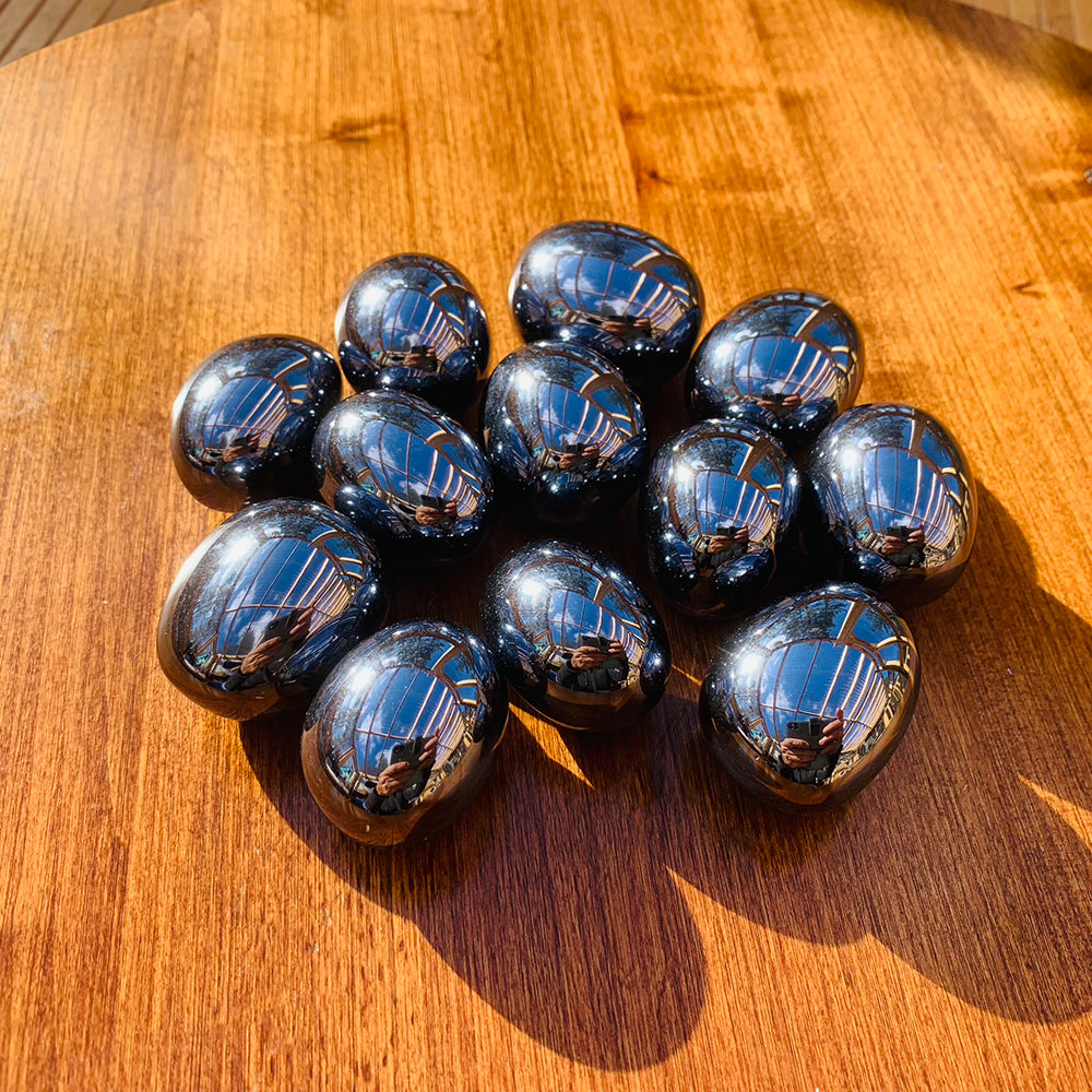 A dozen polished hematite ellipses on a sunlit wooden table, each slightly different in size and sheen