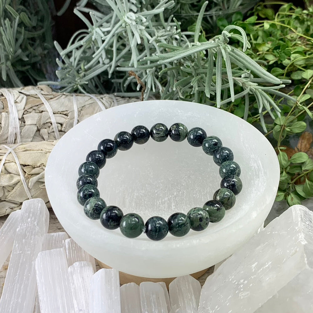 Kambaba jasper mala bracelet of deep green and black patterned beads resting in a selenite bowl