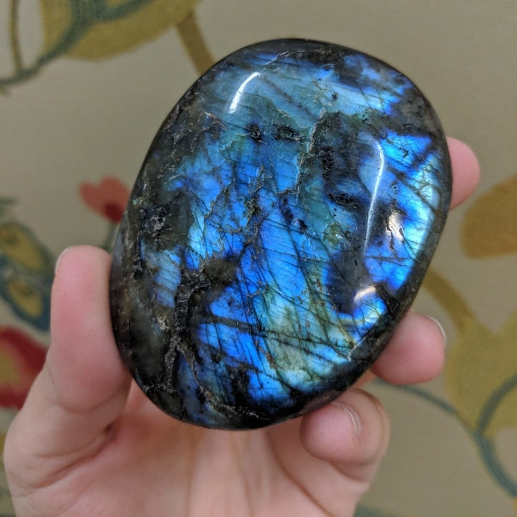 A polished labradorite palm stone flashing bright blue, held in one hand