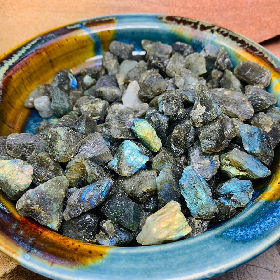 A glazed bowl filled with rough labradorite from our stock, several pieces flashing blue and gold