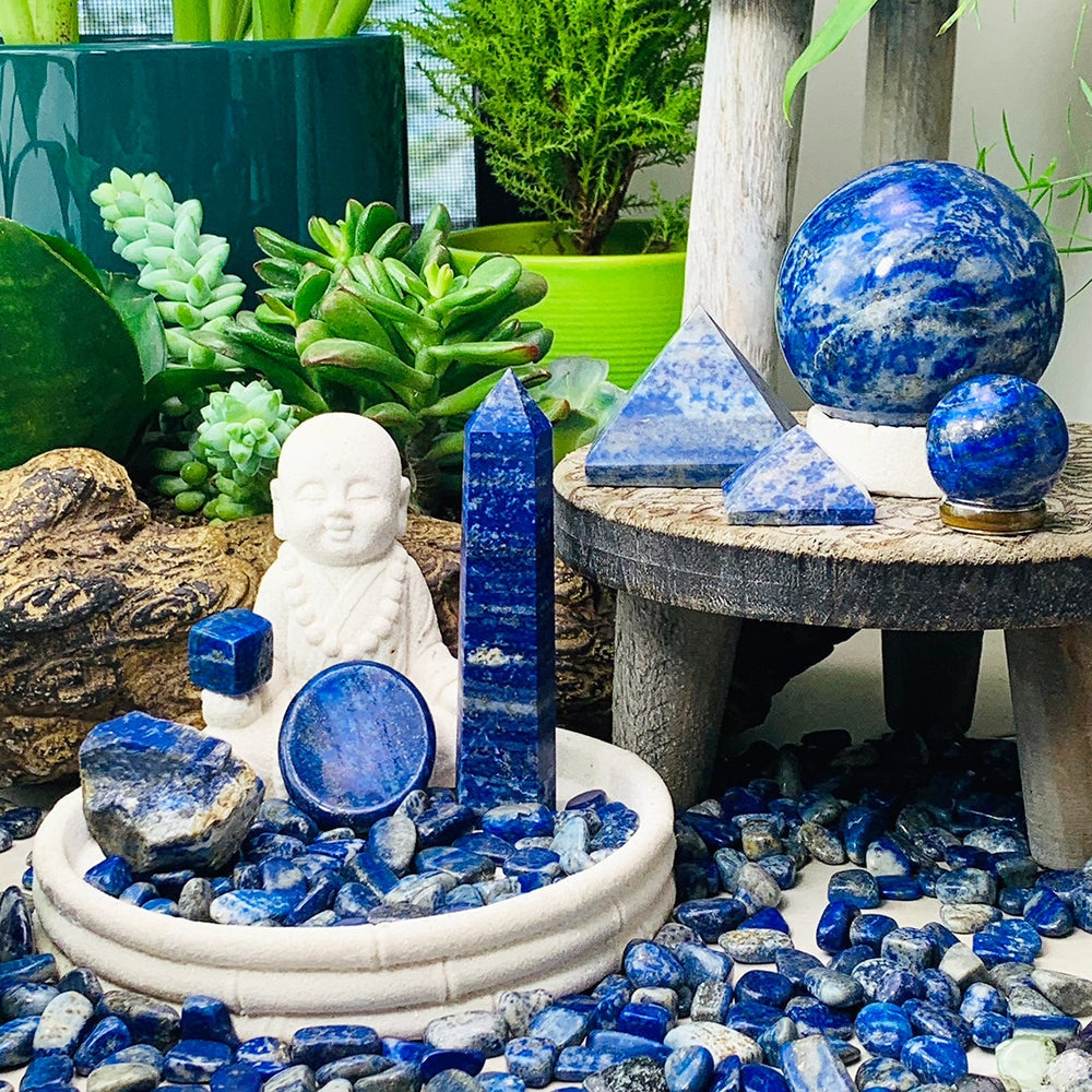 The full lapis lazuli kit arranged together: a point, worry stone, cube and rough stone in a dish, two pyramids and two spheres on a small table, and mini gemstones scattered around