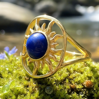 The solar wisdom ring on moss: a round deep blue lapis lazuli cabochon framed by a golden sunburst on an open oval band