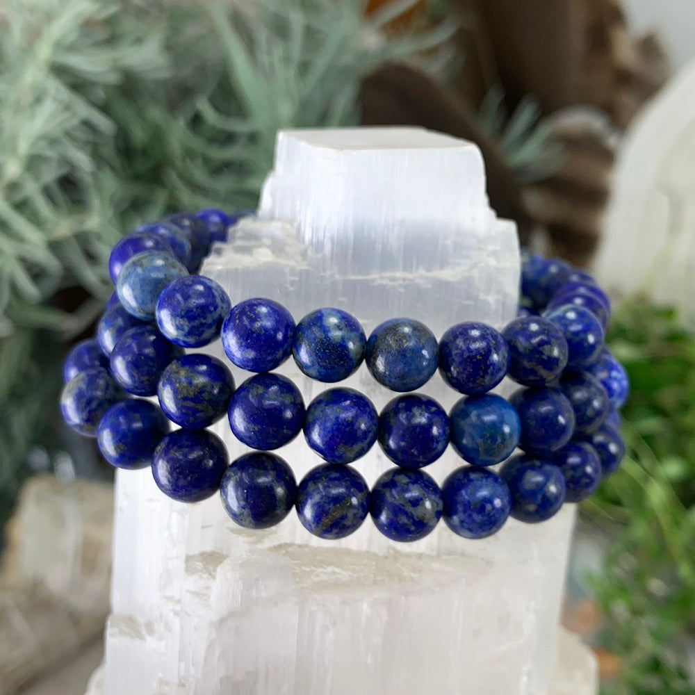 Three lapis lazuli bracelets stacked on a selenite tower, showing the variation from bead to bead