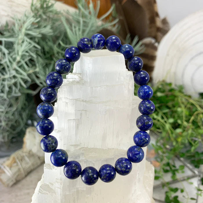 A lapis lazuli mala bracelet of round blue beads draped over a white selenite tower