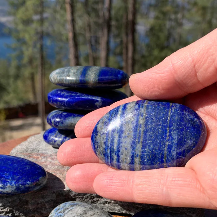 A smooth oval lapis lazuli palm stone held in the palm, with more palm stones stacked behind