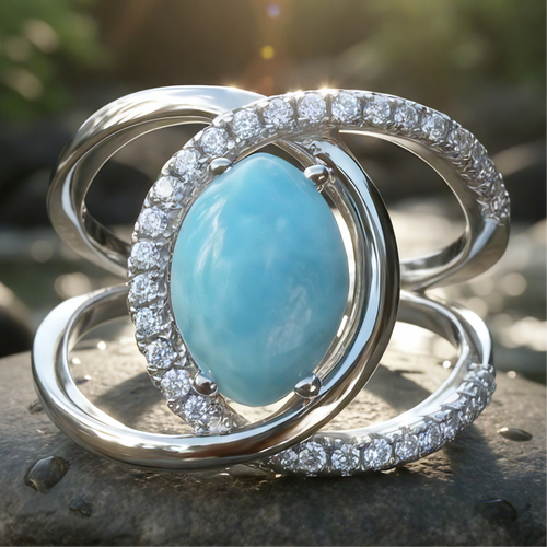 Close-up of the Larimar Radiance Ring: an ocean-blue marbled larimar cabochon ringed by a sweep of sparkling zirconia, with crossing silver bands