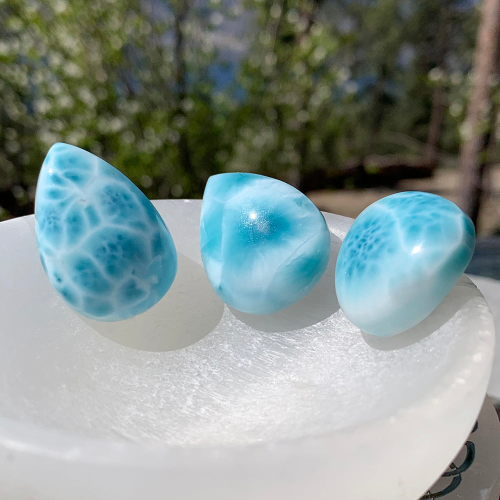 Three Larimar teardrops side by side on a white bowl, each with a different pattern of blue and white
