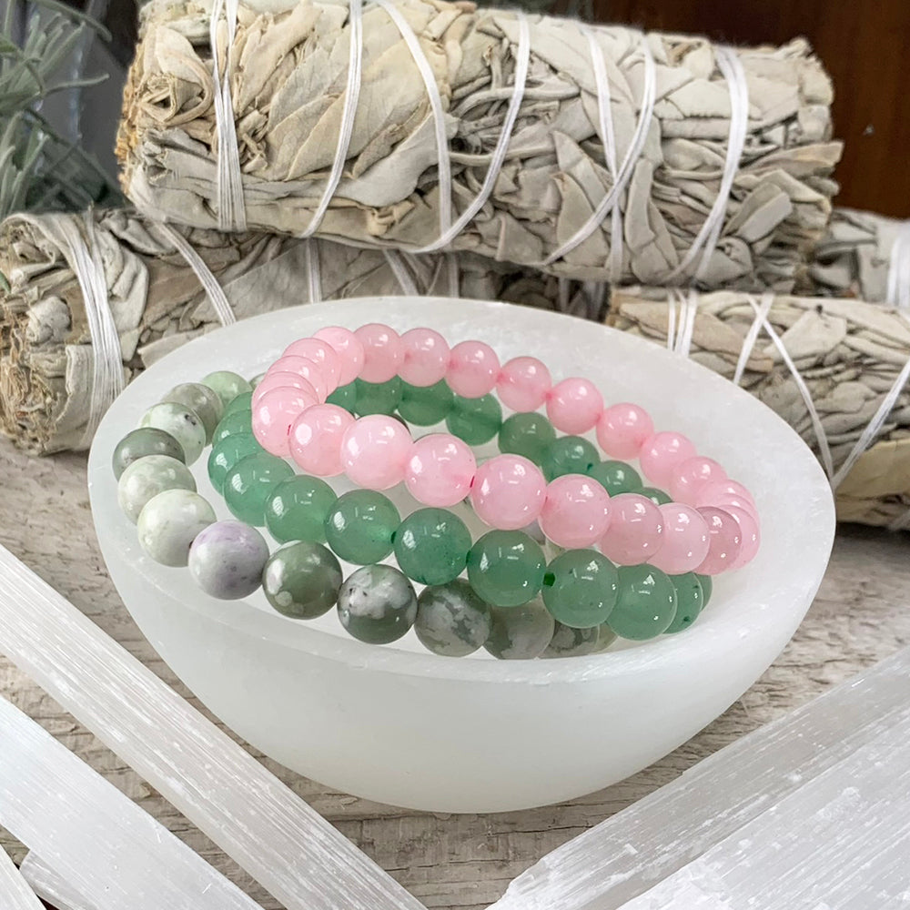 Green aventurine, rose quartz and jade bead bracelets resting together in a white selenite bowl