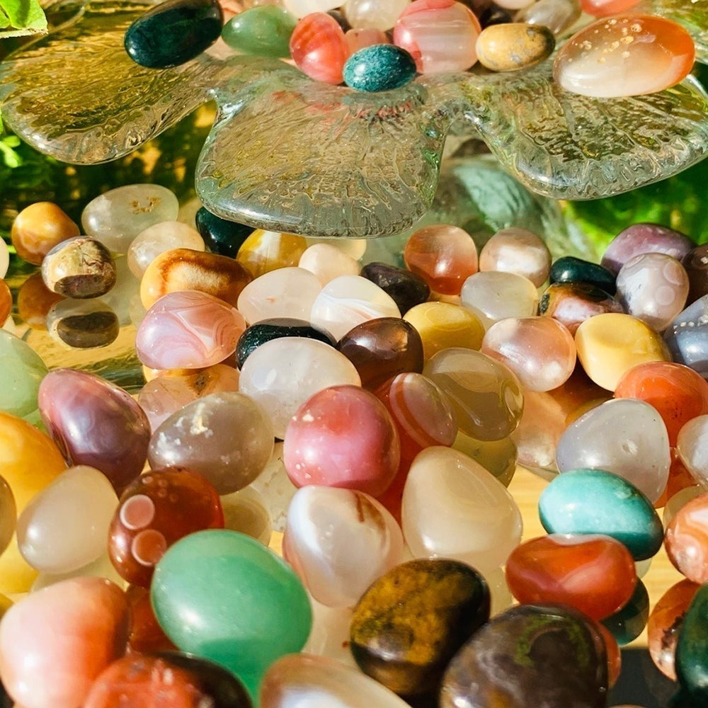 Close-up of polished agate mini gemstones showing their bands and layers in pink, red, cream, green and brown around a glass dish