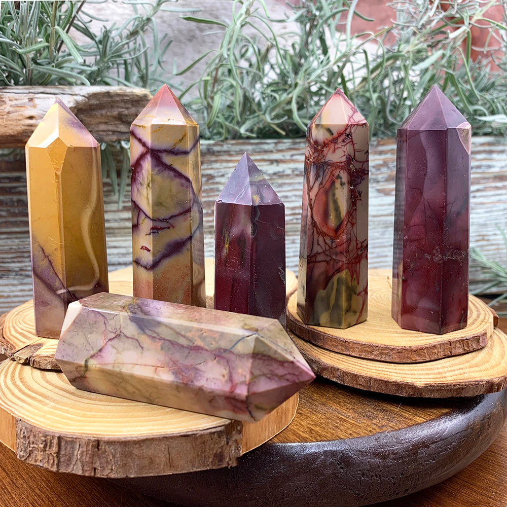 Six polished mookaite points in mustard yellow, ochre, cream, burgundy and purple standing on wood slices
