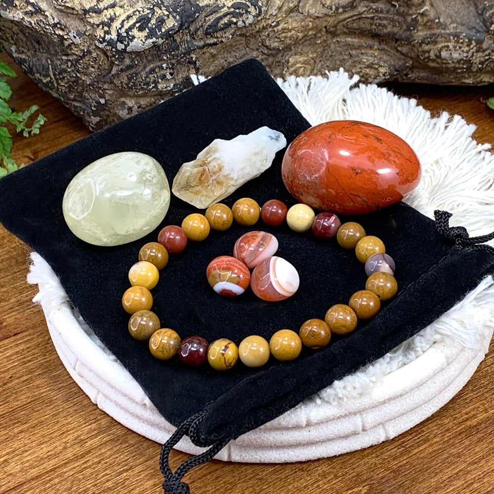 The golden mookaite mala bracelet circling three banded carnelian mini gemstones on a black velvet pouch, with a red jasper tumbled stone, a pale citrine tumbled stone and a citrine shard